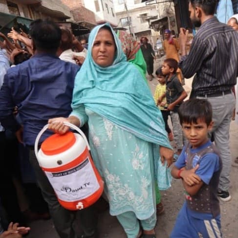 A mother taking home a water cooler with her son beside her