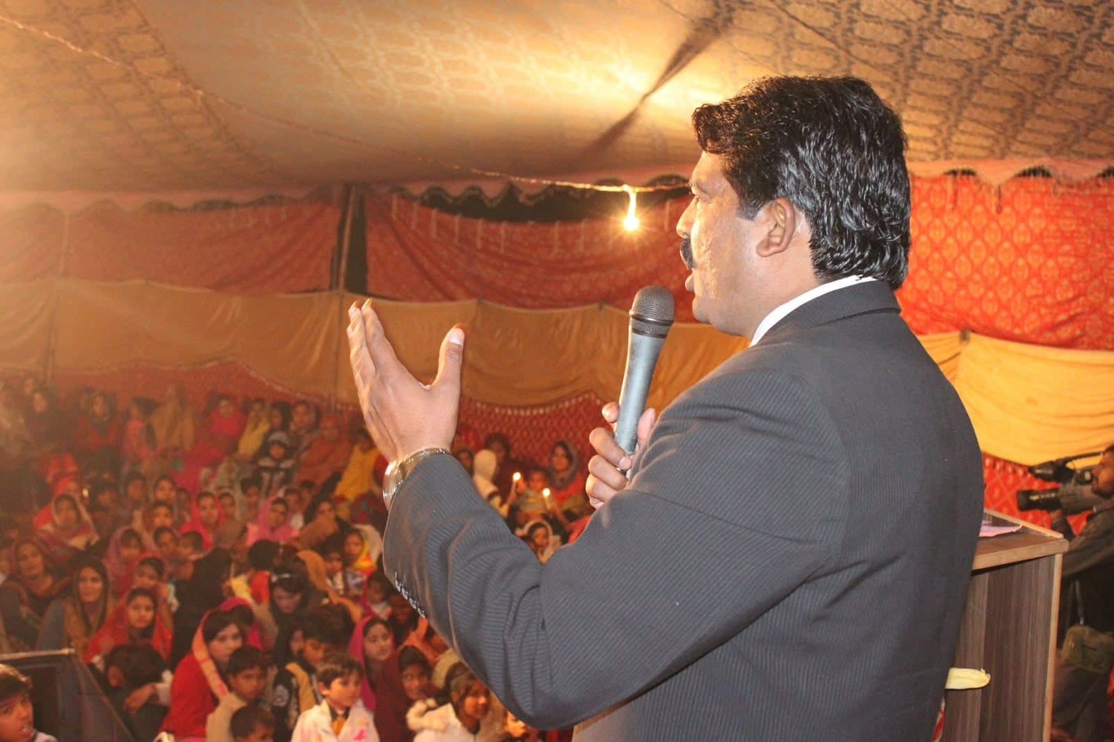 Pastor Arshad Sadiq preaching to a full tent of women and children holding candles