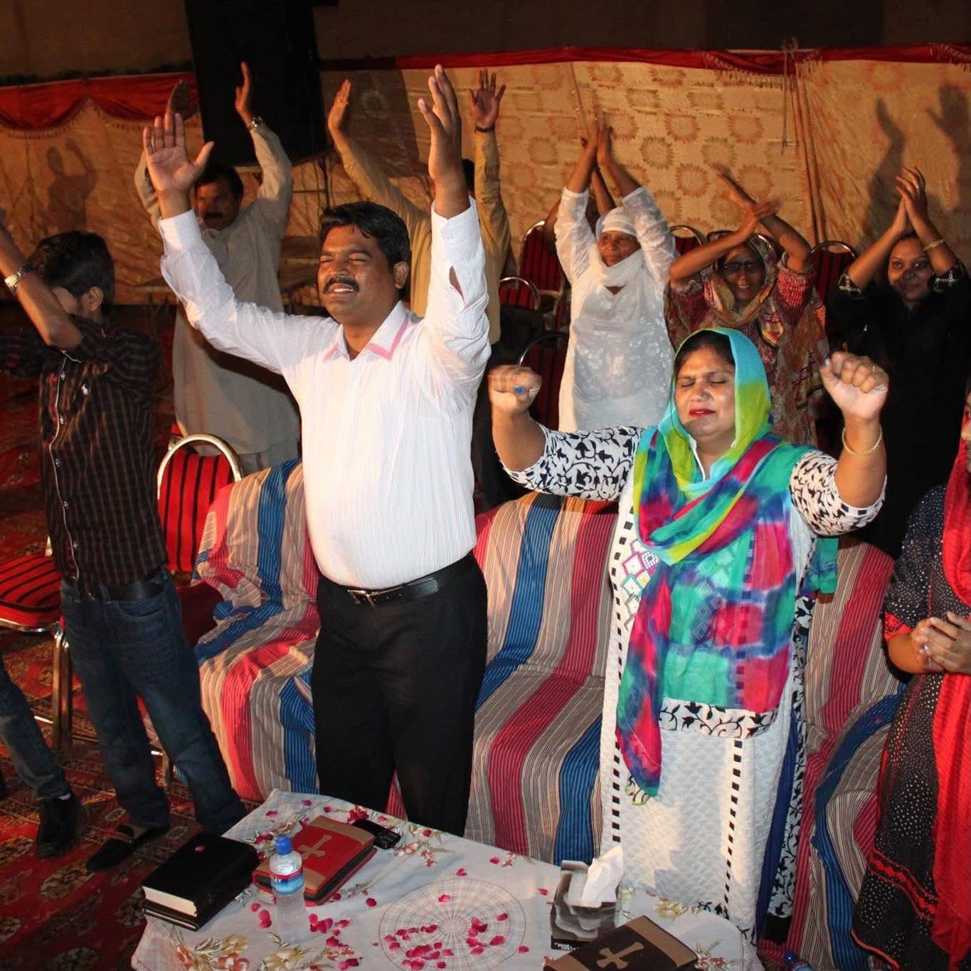 Pastor Arshad Sadiq and the congregation worshipping with hands raised