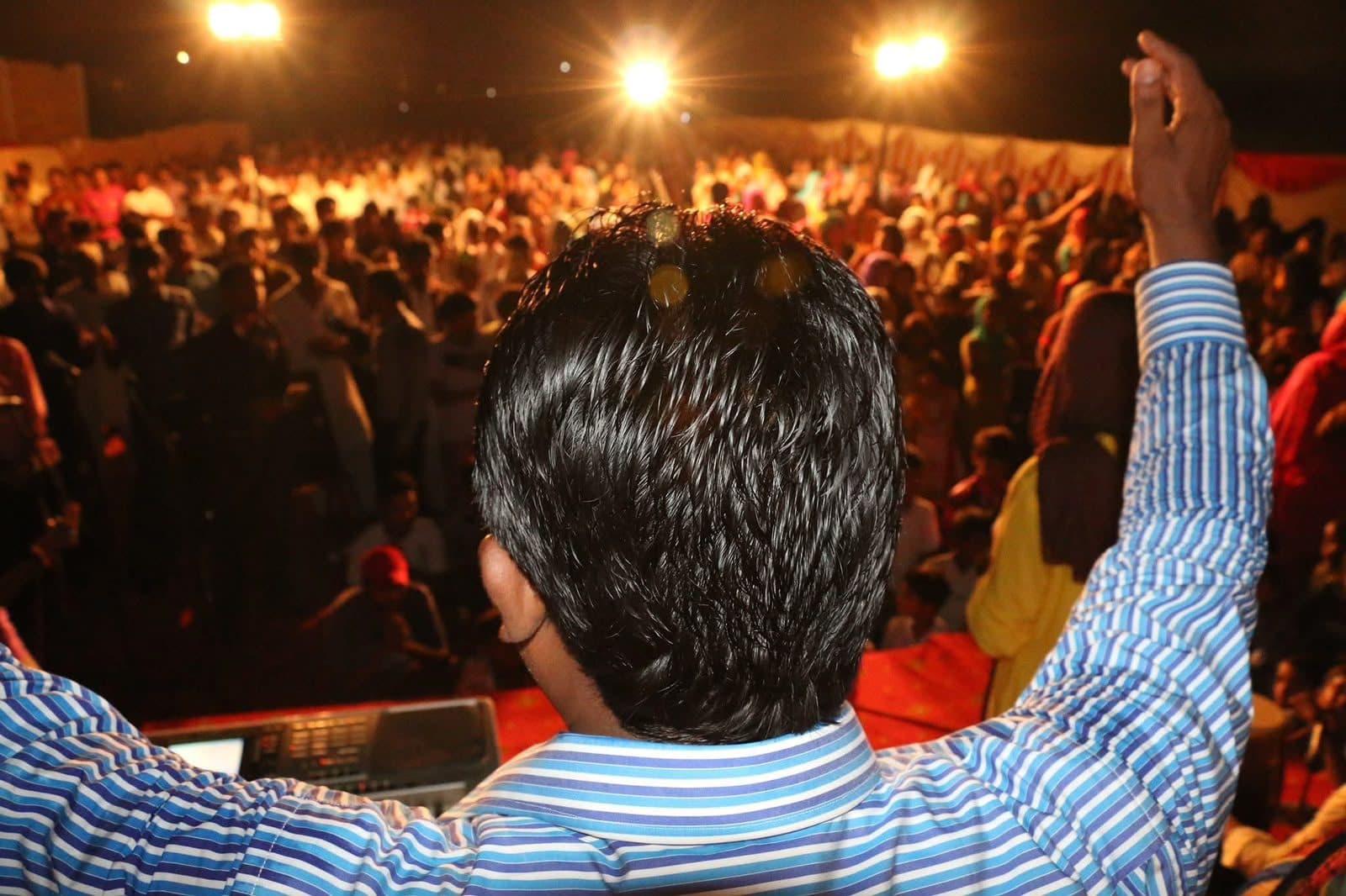 A worship leader on stage lifting a hand over a packed night crusade