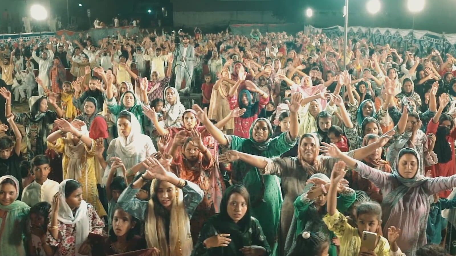 The congregation worshipping with arms raised at a night gathering