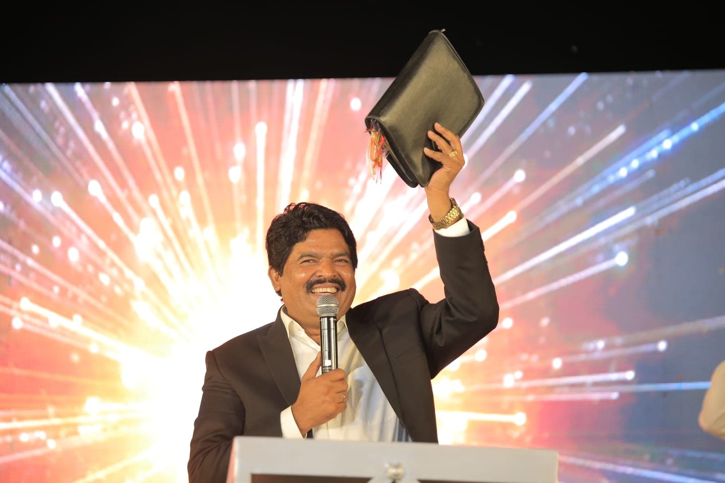 Pastor Arshad Sadiq smiling and holding up his Bible on stage